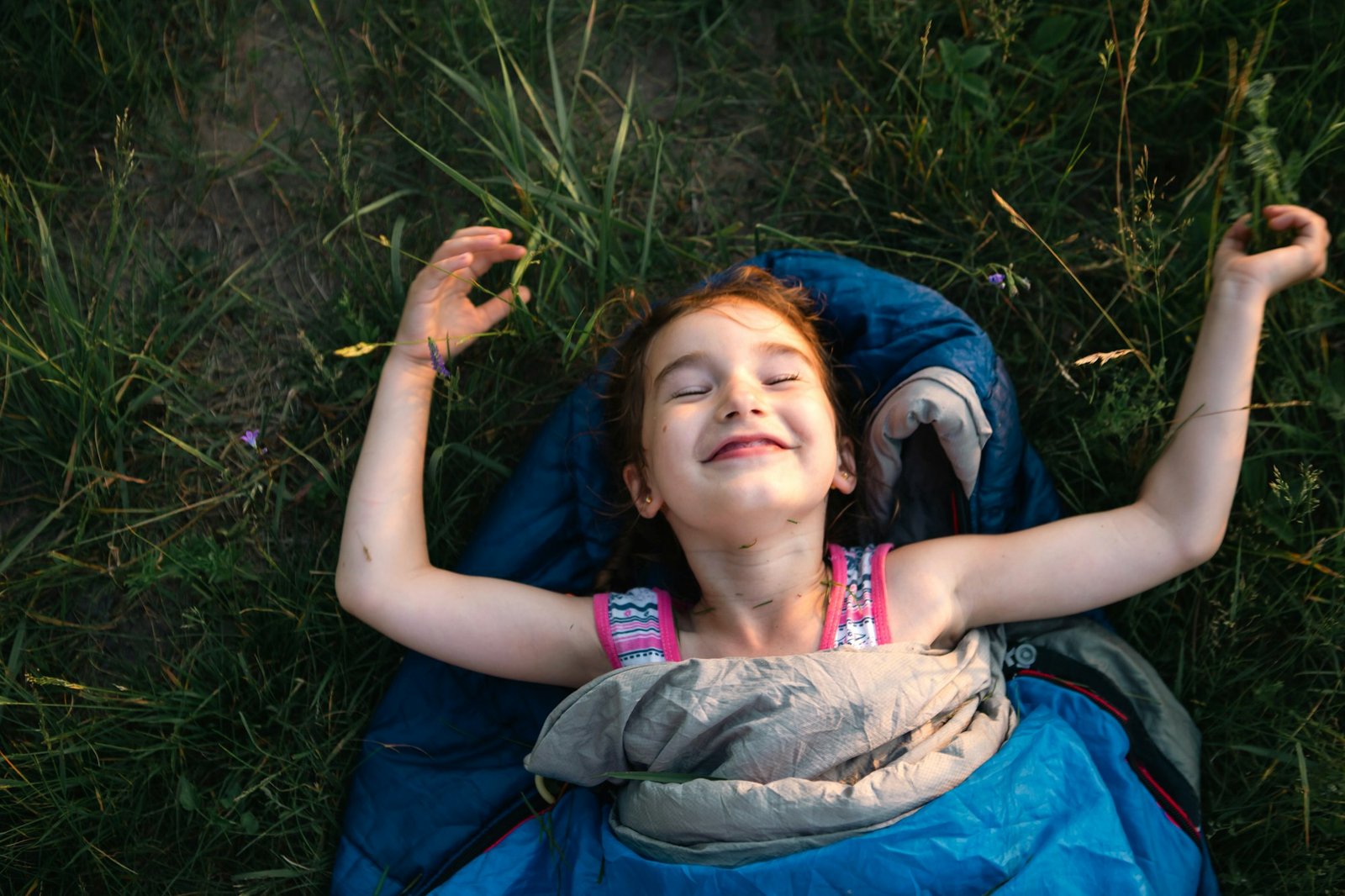 A child sleeps in a sleeping bag on the grass in a camping trip - eco-friendly outdoor